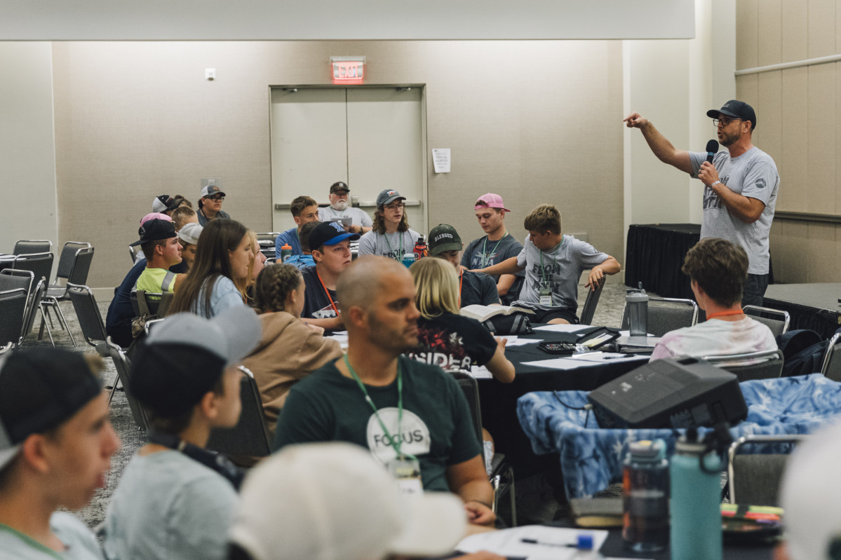 An adult speaking to tables full of teenagers