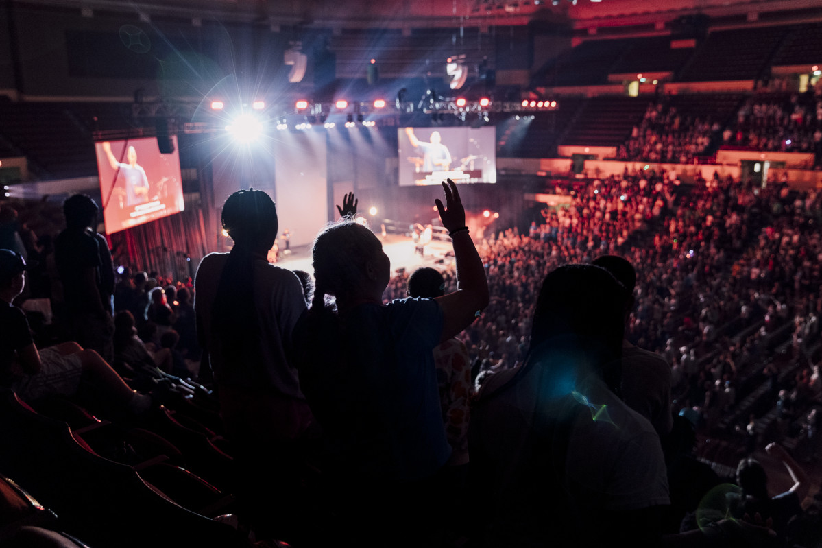 A silhouette of students worshipping in an arena