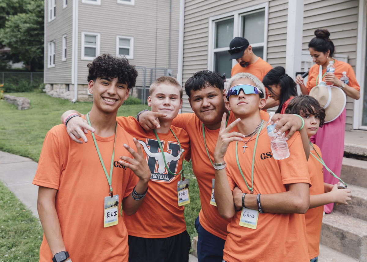 A group of four boys in orange shirts smiling