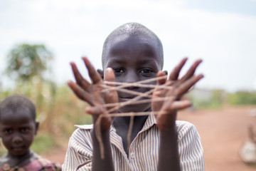 A young child holds up string between his fingers